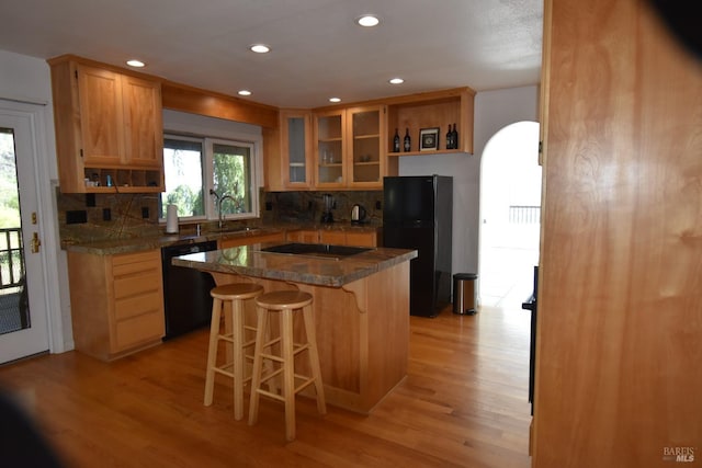 kitchen with light hardwood / wood-style floors, tasteful backsplash, black appliances, sink, and a breakfast bar area