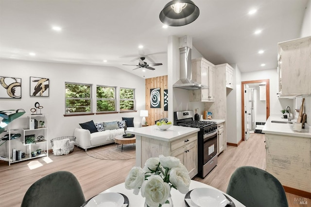 kitchen featuring a sink, open floor plan, light countertops, wall chimney exhaust hood, and stainless steel range with gas stovetop