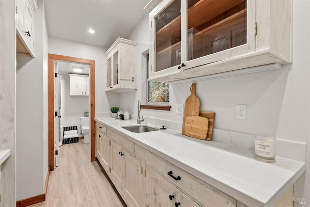 kitchen with recessed lighting, a sink, light countertops, light wood finished floors, and glass insert cabinets