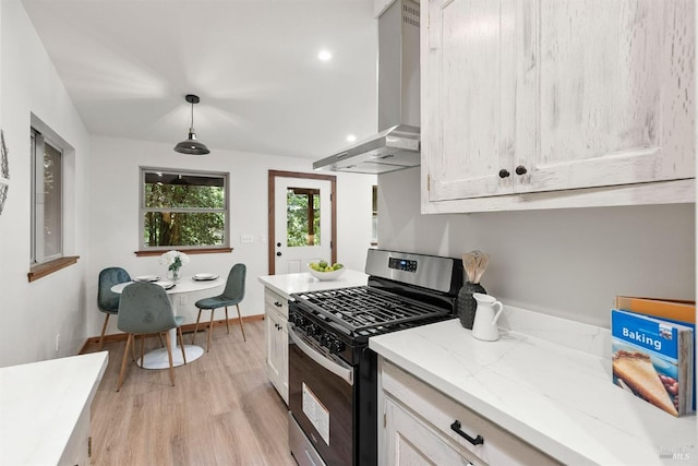 kitchen with hanging light fixtures, stainless steel gas stove, wall chimney range hood, light stone countertops, and light wood-type flooring