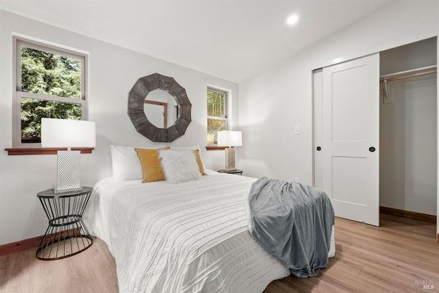 bedroom featuring lofted ceiling, multiple windows, baseboards, and wood finished floors