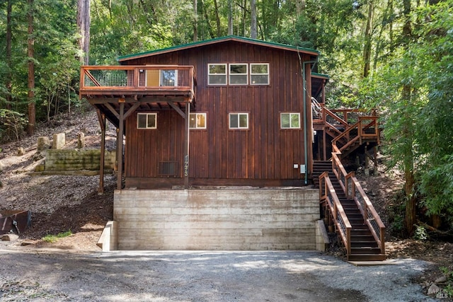 view of front of house featuring a deck, driveway, stairway, and a view of trees