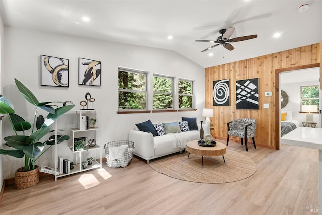 living room with lofted ceiling, light wood-style flooring, recessed lighting, wood walls, and a ceiling fan