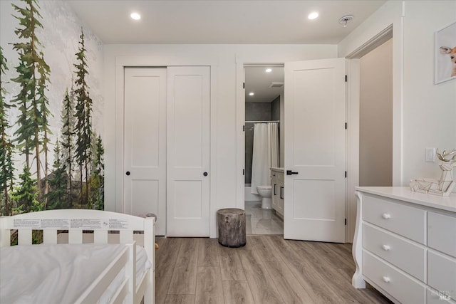 bedroom with connected bathroom, light hardwood / wood-style flooring, and a closet