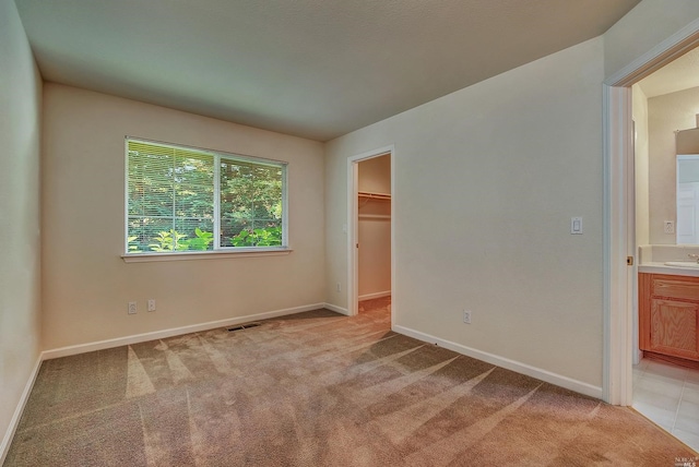 unfurnished bedroom featuring a spacious closet, light carpet, and a closet