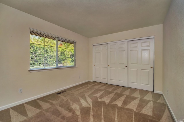 unfurnished bedroom featuring light colored carpet, a textured ceiling, and a closet