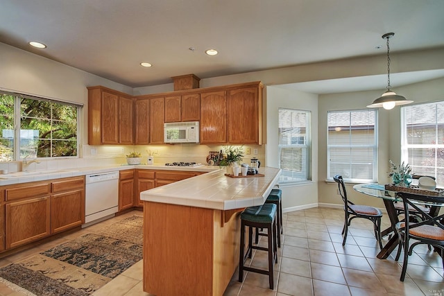 kitchen featuring tile counters, sink, hanging light fixtures, white appliances, and light tile patterned floors