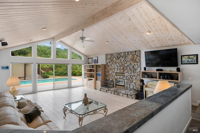 living room featuring high vaulted ceiling, beam ceiling, hardwood / wood-style flooring, a stone fireplace, and ceiling fan