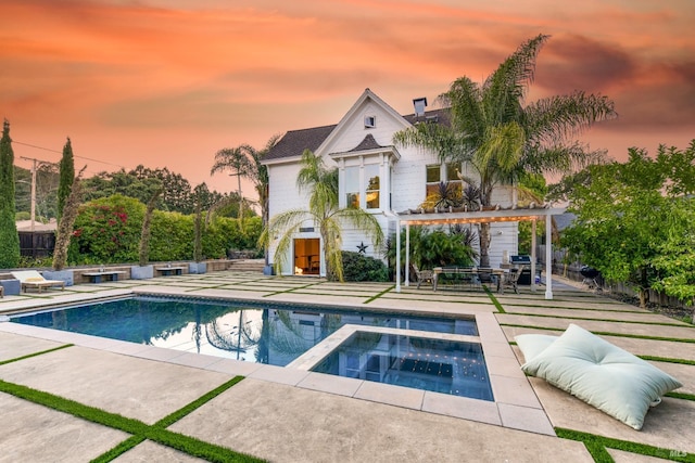 pool at dusk with a pergola, a patio area, and an in ground hot tub