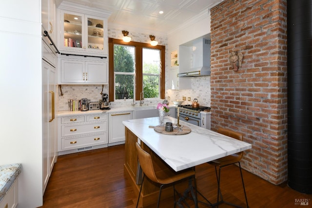 kitchen with high end stainless steel range, a breakfast bar area, backsplash, wall chimney exhaust hood, and sink