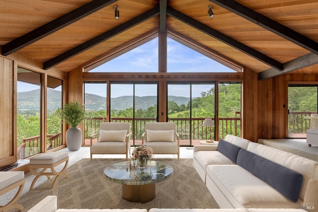 sunroom featuring lofted ceiling with beams, wooden ceiling, a mountain view, and a healthy amount of sunlight