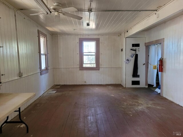 interior space with dark wood-type flooring, ceiling fan, and wood walls