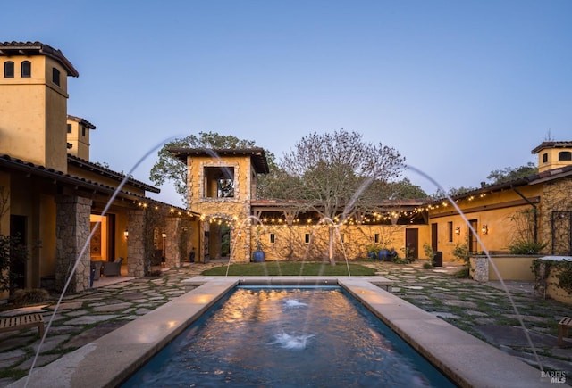 pool at dusk with a patio area and pool water feature