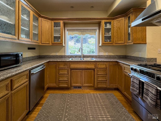 kitchen featuring hardwood / wood-style flooring, wall chimney exhaust hood, stainless steel appliances, dark stone counters, and sink