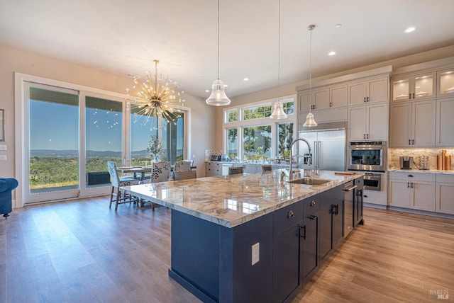 kitchen featuring tasteful backsplash, light hardwood / wood-style flooring, an island with sink, and decorative light fixtures