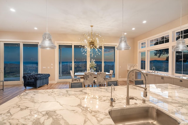 kitchen featuring decorative light fixtures, light hardwood / wood-style floors, light stone counters, and sink