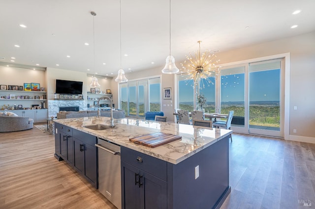 kitchen featuring light stone counters, stainless steel dishwasher, hanging light fixtures, and an island with sink