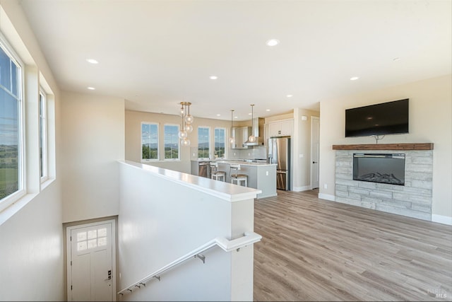 kitchen with stainless steel appliances, wall chimney range hood, light hardwood / wood-style flooring, decorative backsplash, and a kitchen island