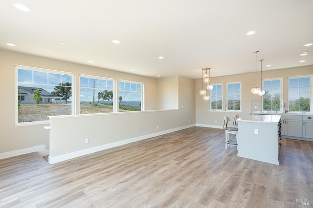 kitchen with appliances with stainless steel finishes, light wood-type flooring, wall chimney range hood, pendant lighting, and a kitchen island