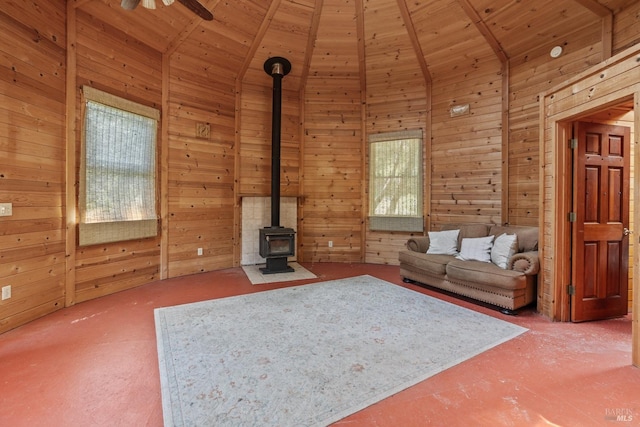 unfurnished living room with ceiling fan, high vaulted ceiling, wooden walls, wooden ceiling, and a wood stove