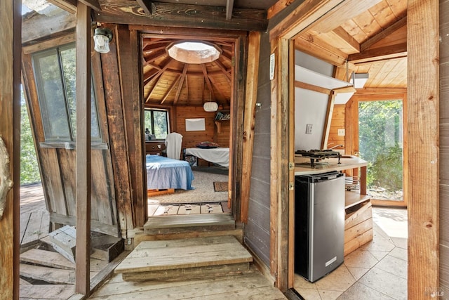 hall with vaulted ceiling, wood walls, and a wealth of natural light