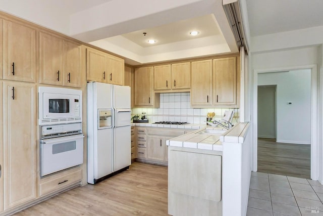 kitchen with backsplash, light wood-type flooring, tile counters, sink, and white appliances