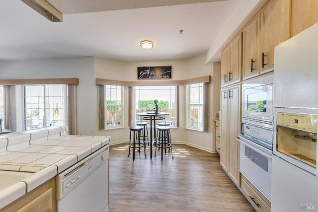 kitchen with light brown cabinets, hardwood / wood-style floors, tile countertops, beamed ceiling, and white appliances