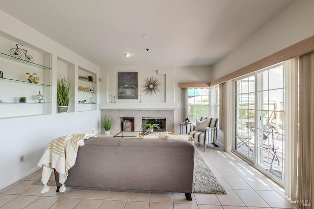 living room with a tiled fireplace, built in shelves, and light tile floors