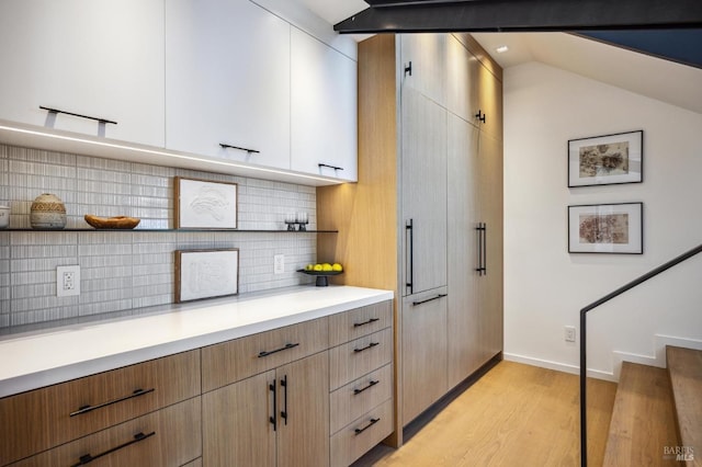 kitchen with tasteful backsplash, white cabinetry, lofted ceiling, and light hardwood / wood-style floors