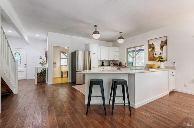 kitchen featuring stainless steel refrigerator, dark hardwood / wood-style floors, kitchen peninsula, white cabinetry, and pendant lighting