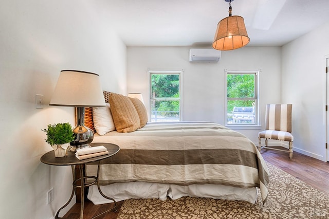 bedroom featuring multiple windows, wood finished floors, baseboards, and a wall mounted air conditioner