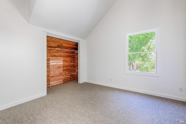 empty room featuring carpet flooring, wood walls, baseboards, and vaulted ceiling