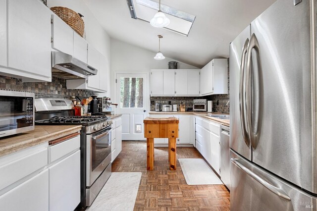 kitchen with wall chimney range hood, hanging light fixtures, appliances with stainless steel finishes, parquet flooring, and backsplash