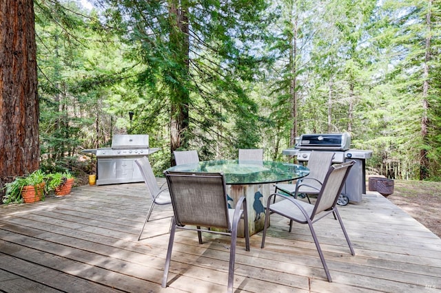 wooden terrace featuring outdoor dining space, a forest view, and a grill