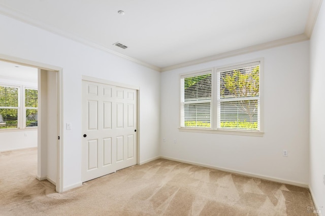 unfurnished bedroom featuring light carpet, baseboards, visible vents, ornamental molding, and a closet