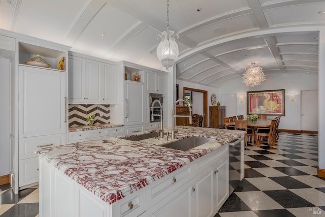 kitchen featuring hanging light fixtures, lofted ceiling with beams, an island with sink, backsplash, and dark tile floors