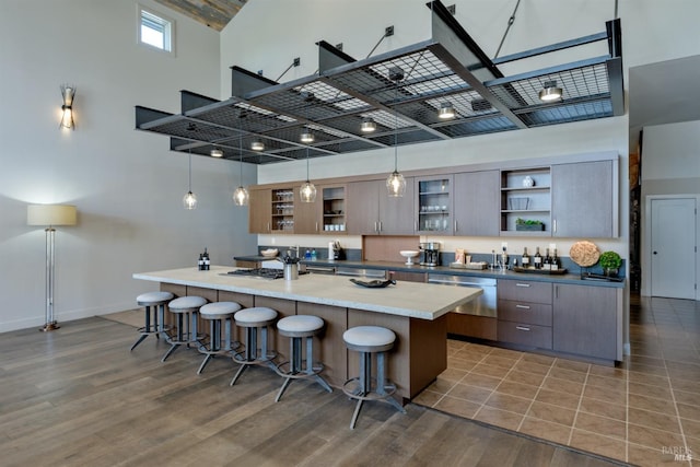 kitchen with hanging light fixtures, an island with sink, a breakfast bar area, hardwood / wood-style floors, and a high ceiling