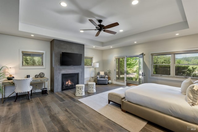 bedroom featuring a large fireplace, dark hardwood / wood-style flooring, ceiling fan, and a raised ceiling