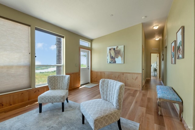 living area featuring light wood-type flooring, wood walls, and vaulted ceiling