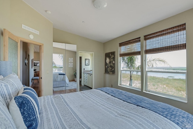 bedroom featuring connected bathroom, vaulted ceiling, multiple windows, and hardwood / wood-style flooring