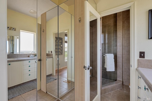 bathroom with a tile shower, tile patterned floors, a textured ceiling, and vanity