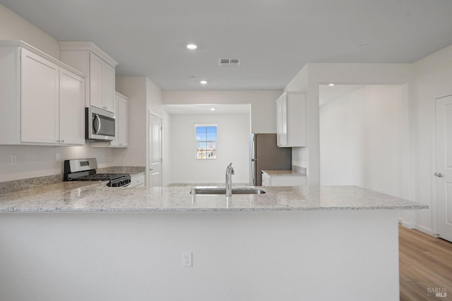 kitchen featuring sink, light wood-type flooring, appliances with stainless steel finishes, white cabinetry, and kitchen peninsula