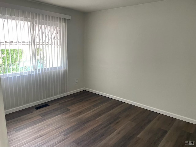 empty room featuring dark wood-style flooring, visible vents, and baseboards