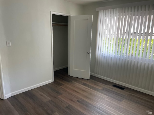 unfurnished bedroom with dark wood-style flooring, a closet, visible vents, and baseboards