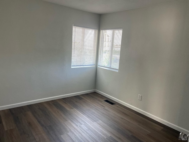 empty room with visible vents, baseboards, and dark wood-style flooring