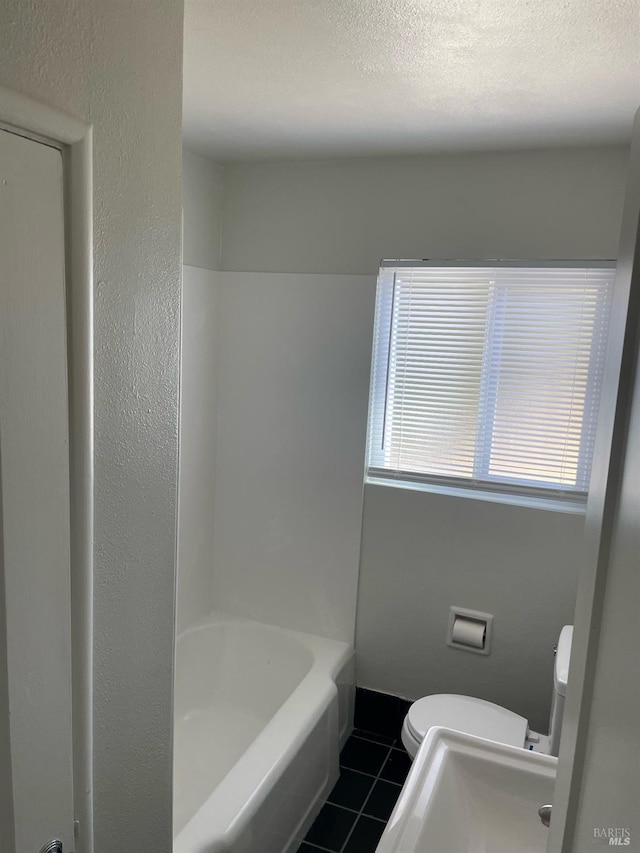 bathroom featuring a textured wall, toilet, a textured ceiling, baseboards, and tile patterned floors