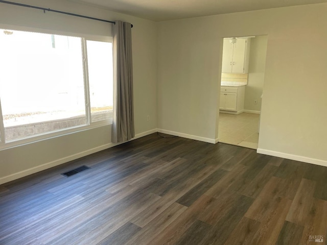 unfurnished room featuring dark wood-type flooring, visible vents, and baseboards