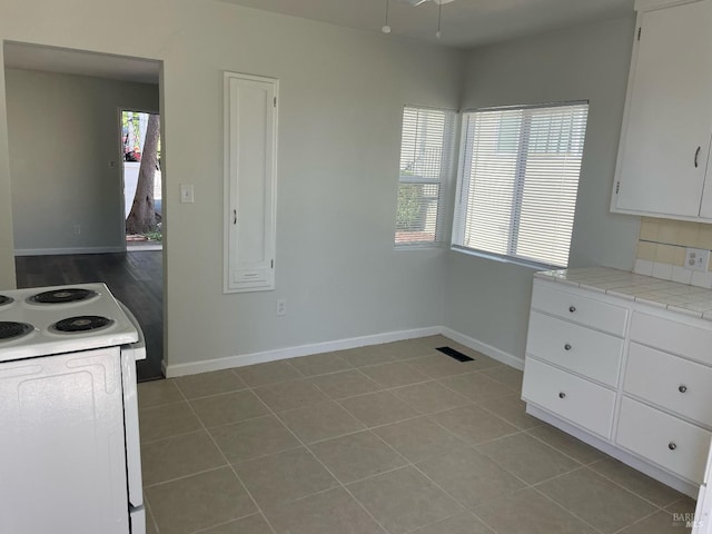 kitchen with tile countertops, a wealth of natural light, white cabinets, and white electric range