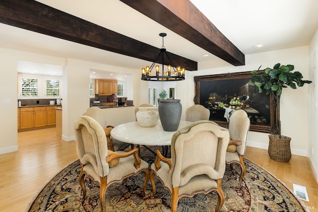 dining area with light wood-type flooring, a chandelier, and beamed ceiling