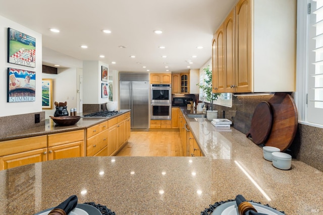 kitchen with appliances with stainless steel finishes, light brown cabinetry, sink, and light stone countertops